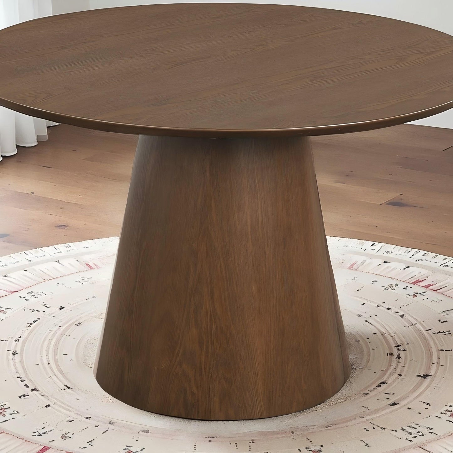 Round wooden dining table with conical base on patterned rug in modern home setting