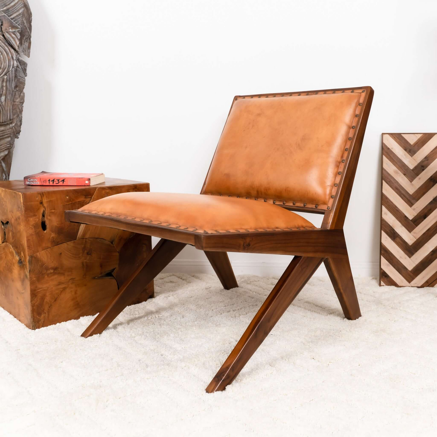 Modern brown leather accent chair with wooden frame on white rug, next to wood side table.