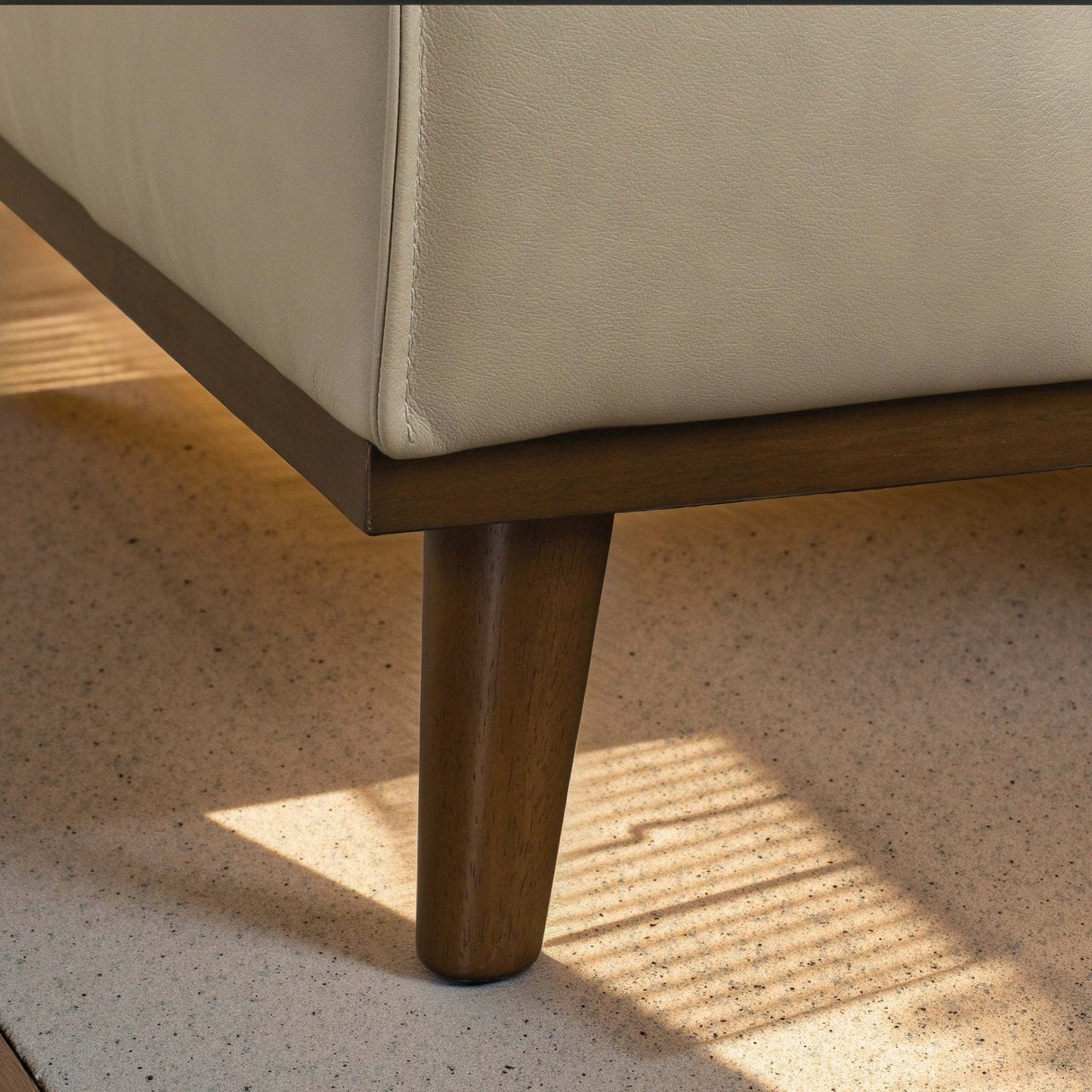 Modern beige leather sofa corner with wooden leg on light speckled flooring