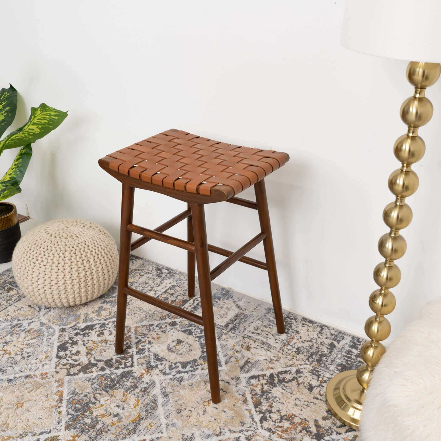 Woven leather seat wooden barstool on a patterned rug with decor in a modern home setting