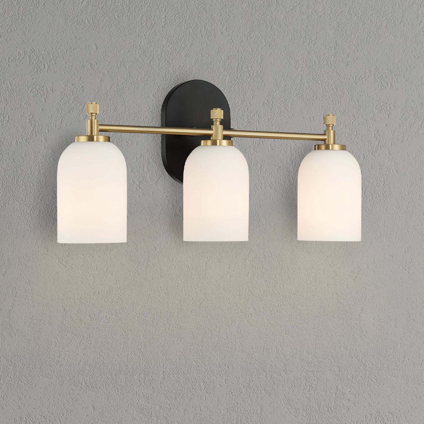 Modern three-light wall sconce with frosted glass shades and brass accents on gray wall