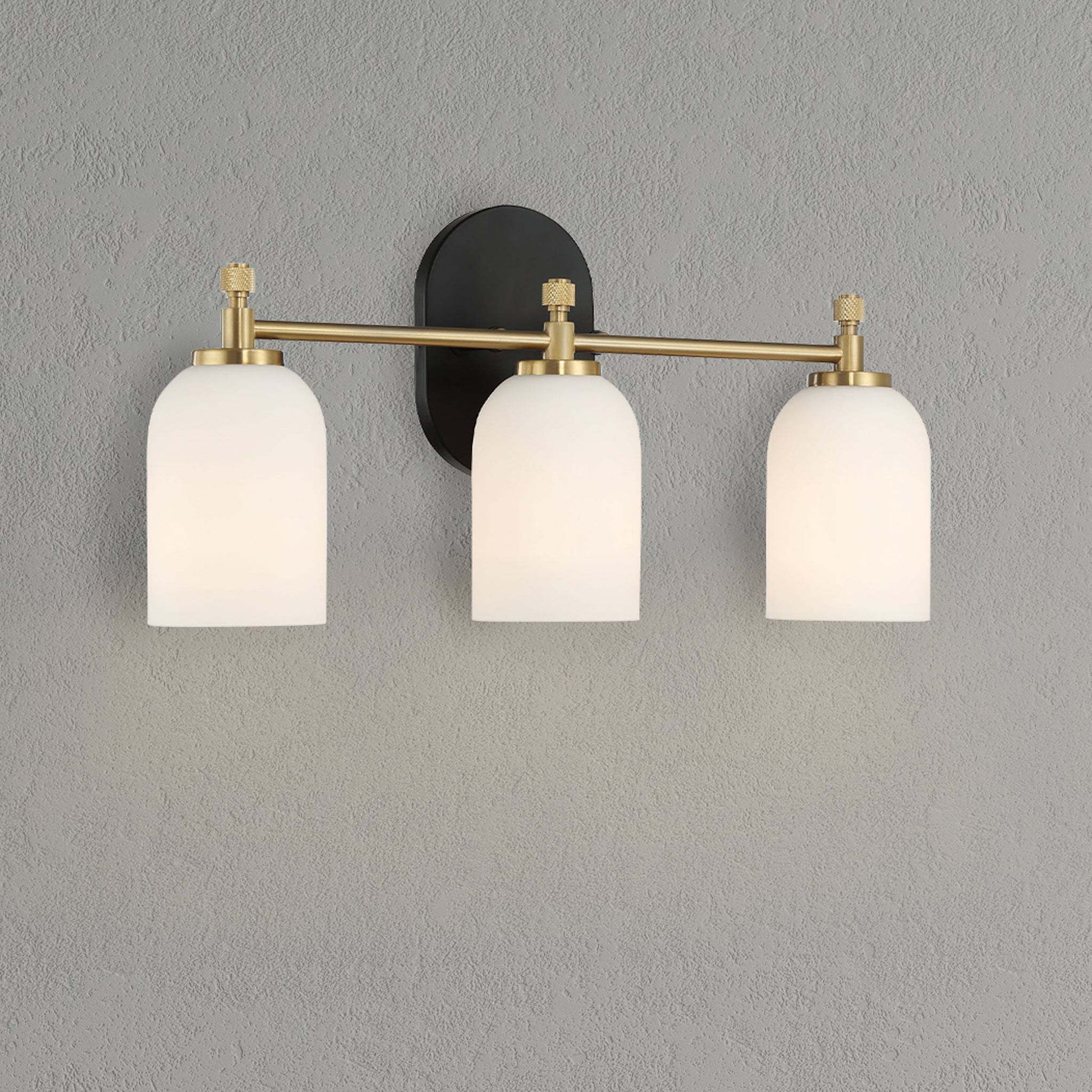 Modern three-light wall sconce with frosted glass shades and brass accents on gray wall
