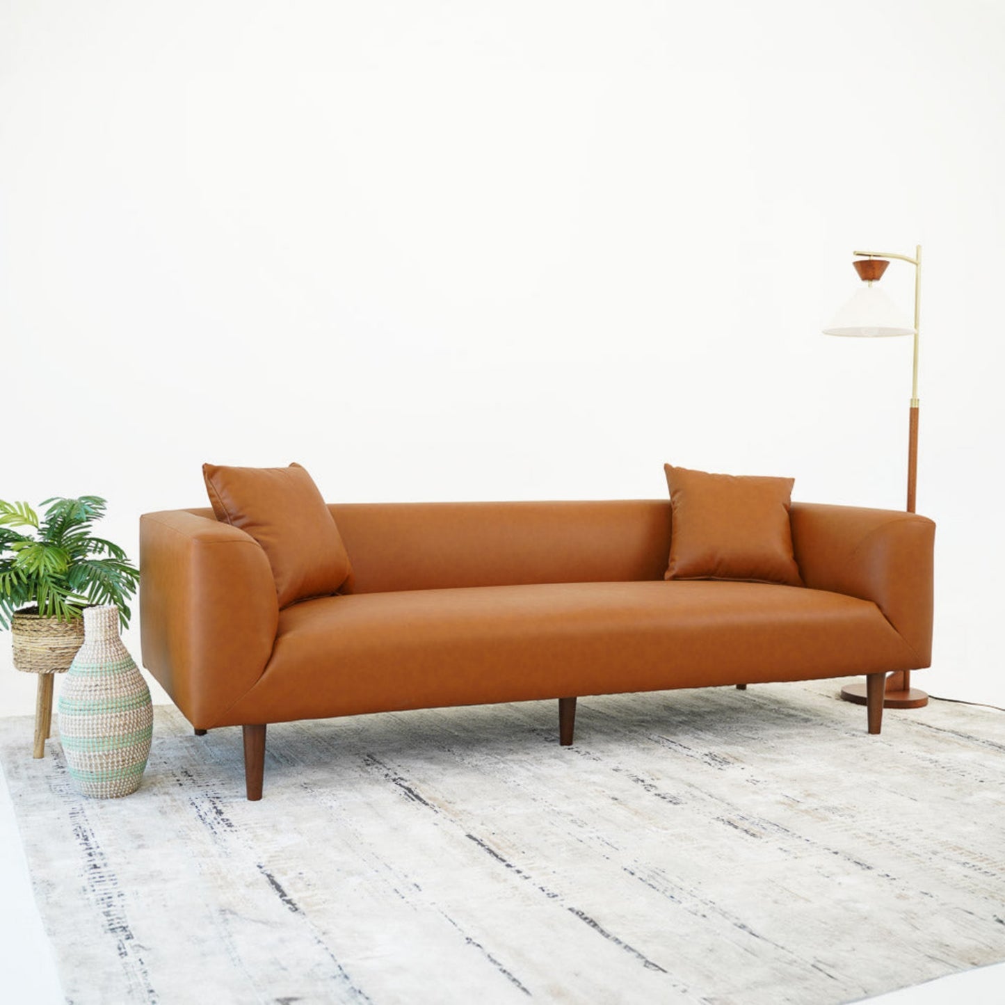 Modern brown leather sofa with two cushions on a light rug, styled with a floor lamp and indoor plant