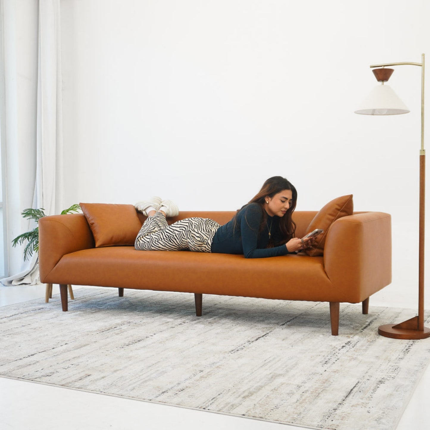 Modern brown leather sofa with woman relaxing, reading on phone in bright living room