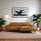 Modern living room with tan leather sectional sofa, indoor plants, and framed wall art