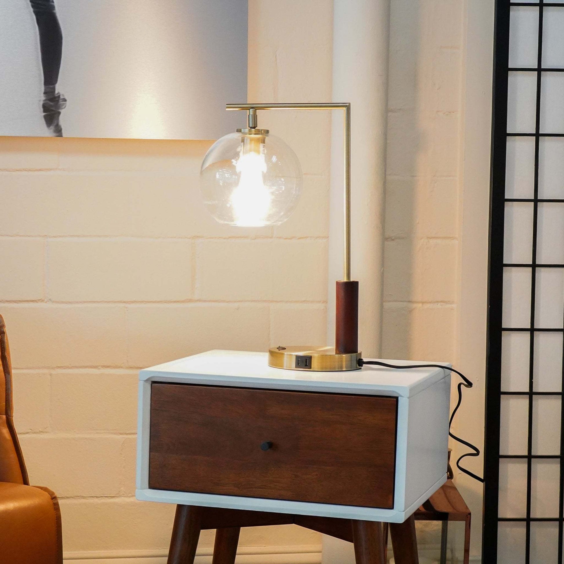 Modern brass table lamp with glass globe on wood nightstand in stylish living room