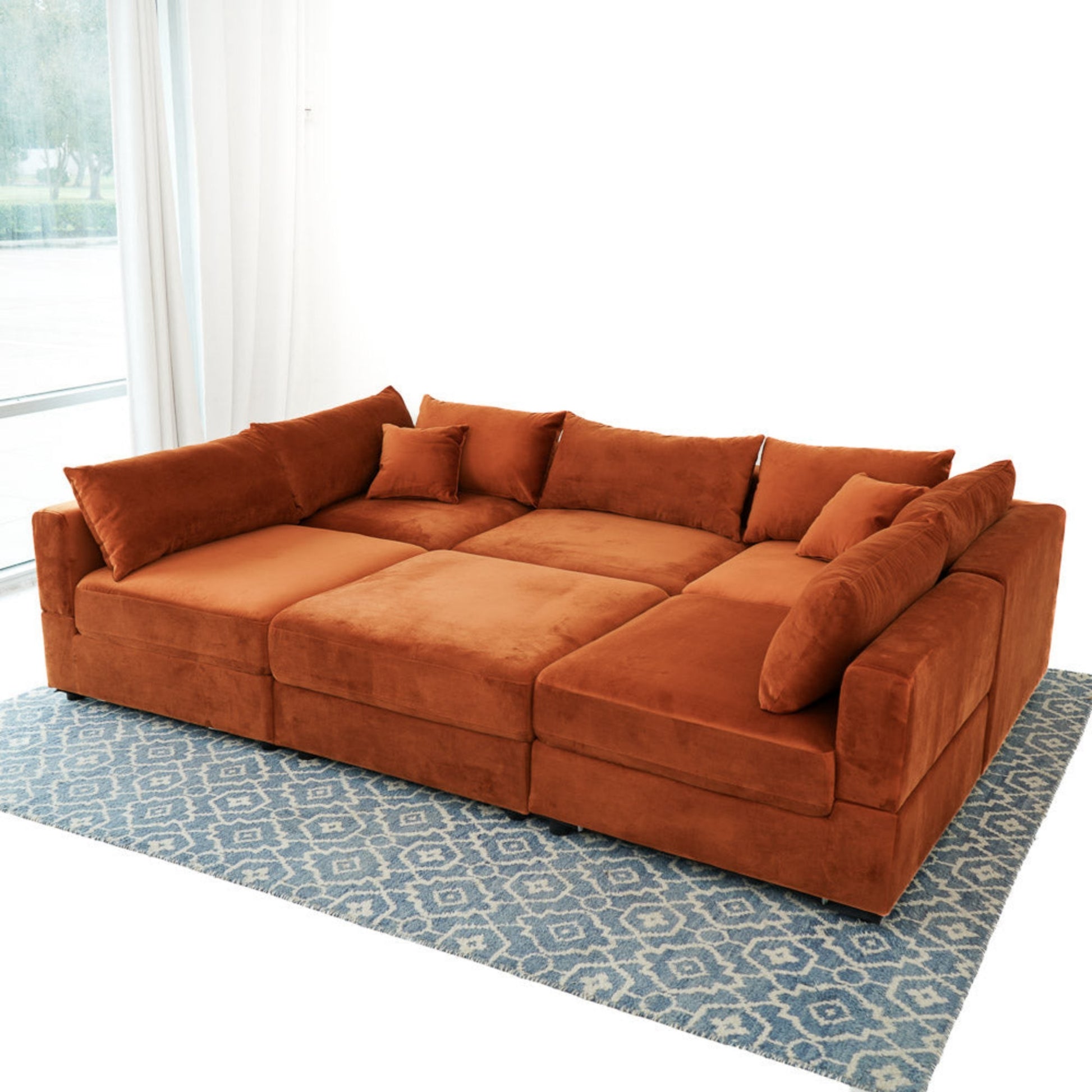 Large rust orange sectional sofa with plush cushions on a blue patterned rug in a bright living room