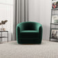 Modern green velvet armchair in a bright living room with a textured rug, bookshelf, and side table.
