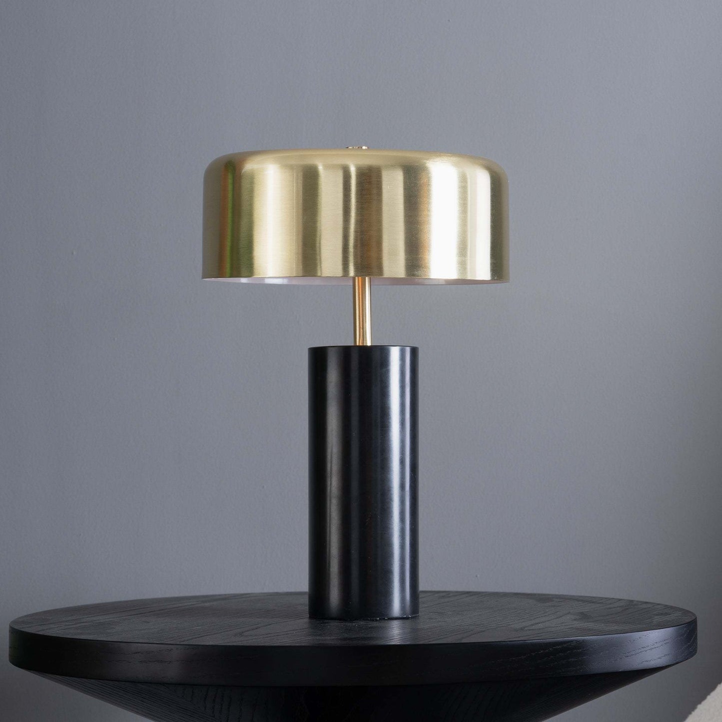 Modern brass and black table lamp on dark round wooden table, home furniture decor