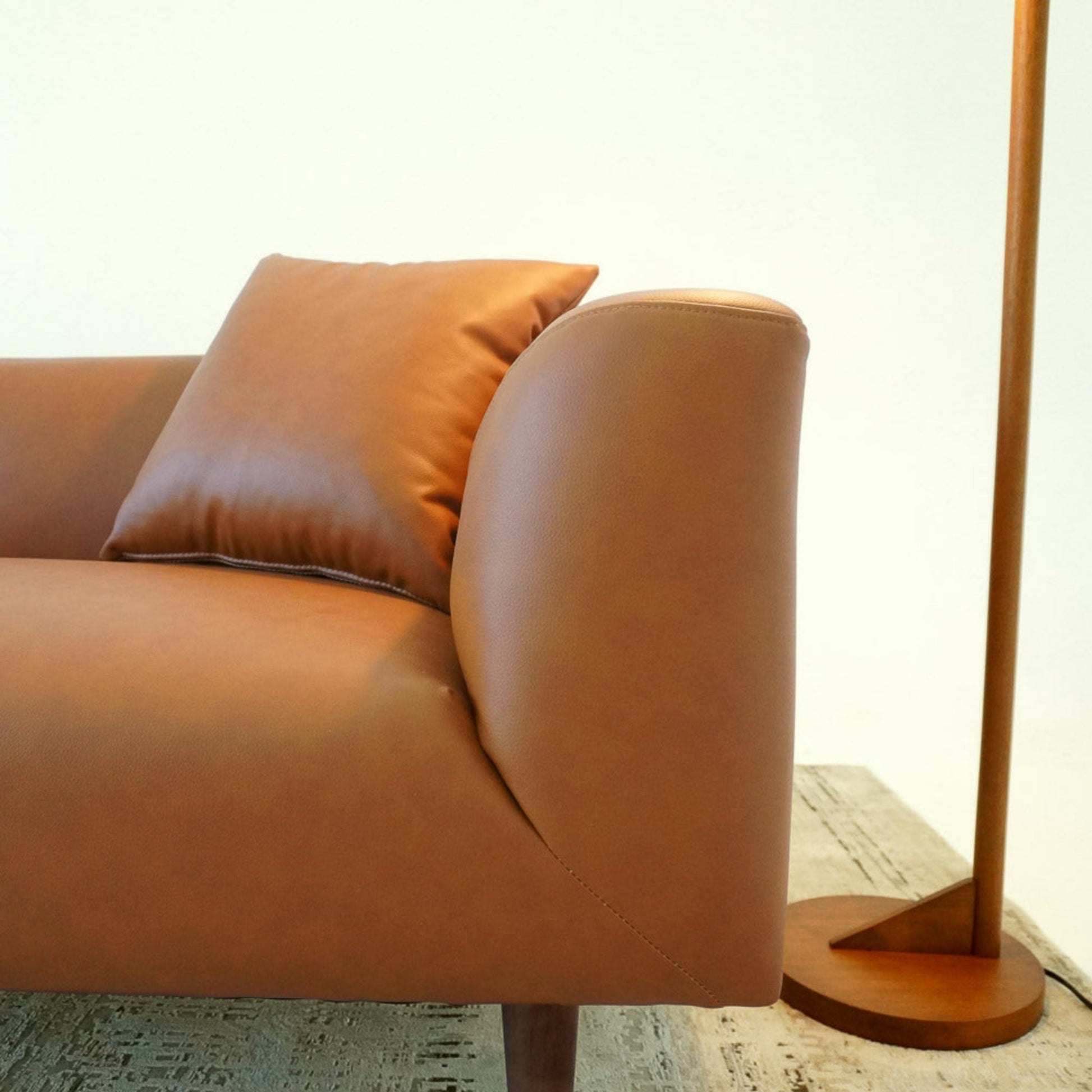 Modern brown leather sofa with cushion and wooden floor lamp on neutral rug