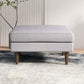 Modern light gray upholstered ottoman with wooden legs on a textured rug