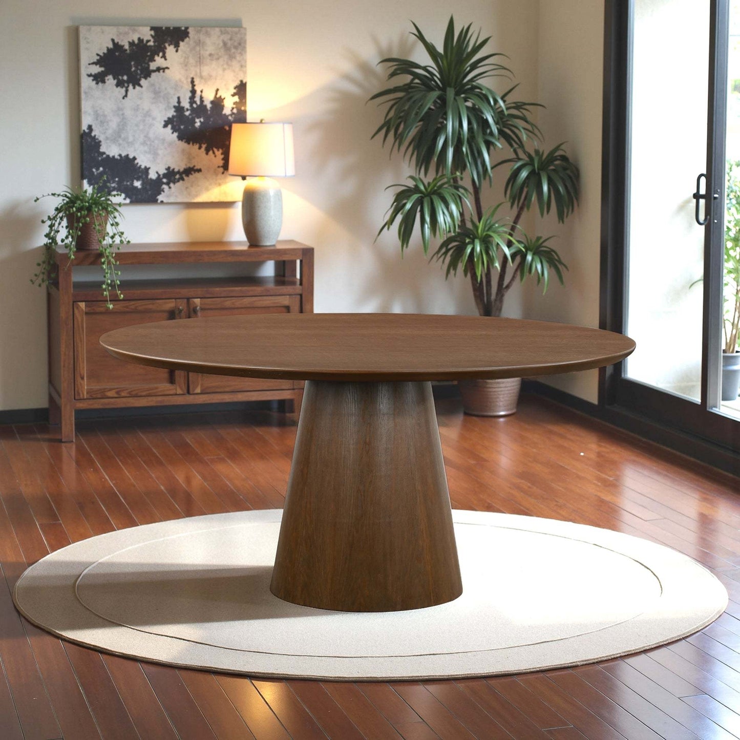 Modern round wooden dining table on white rug in bright living room with plants, lamp, and sideboard