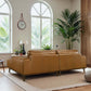 Modern living room with tan leather sofa, potted plants, large windows, and neutral decor