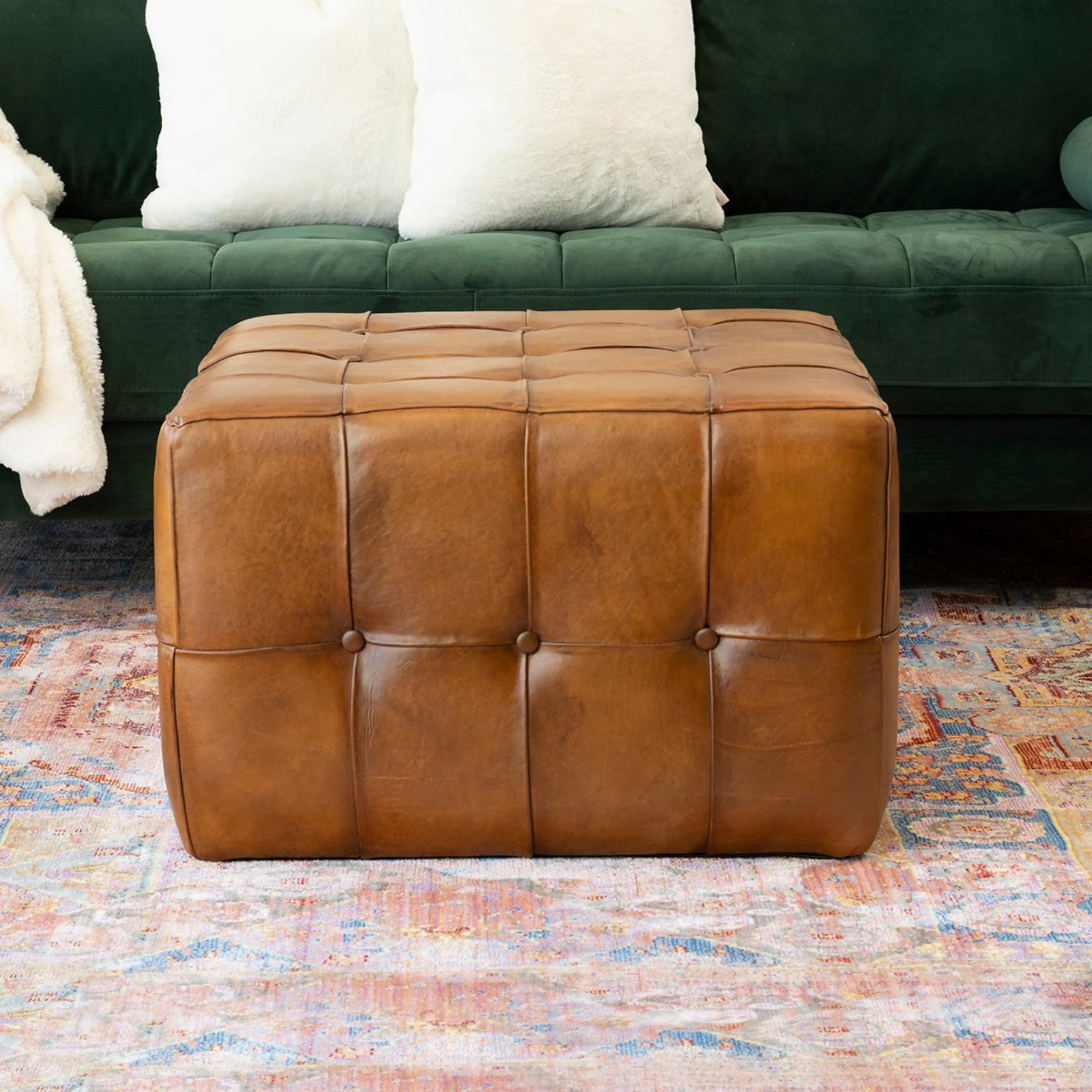 Brown leather ottoman on colorful rug in front of green sofa with white pillows