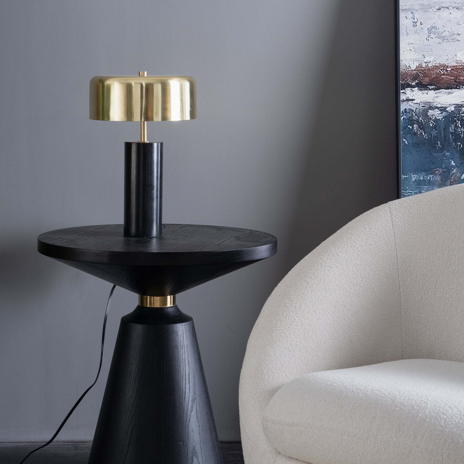 Modern black side table with gold lamp beside a white upholstered chair in a stylish living room
