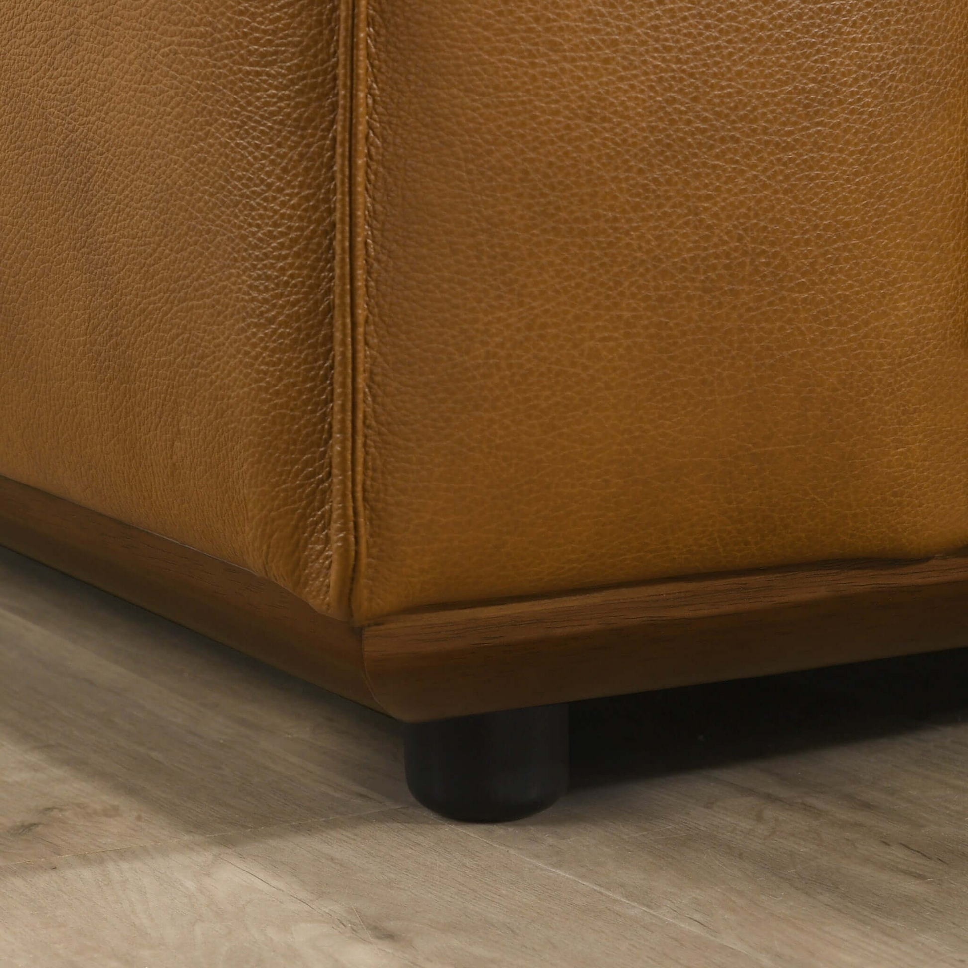 Close-up of brown leather sofa corner with wood base on hardwood floor, FredCo International furniture