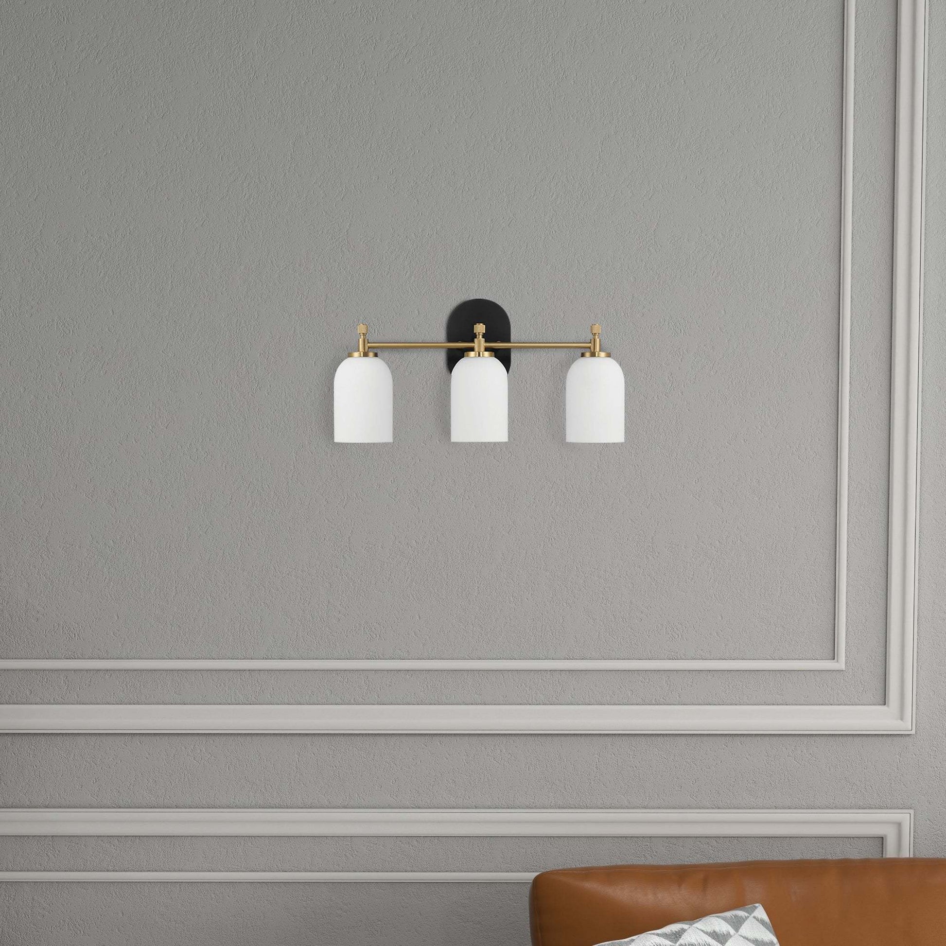 Modern triple wall sconce with white shades above a brown leather sofa on gray paneled wall