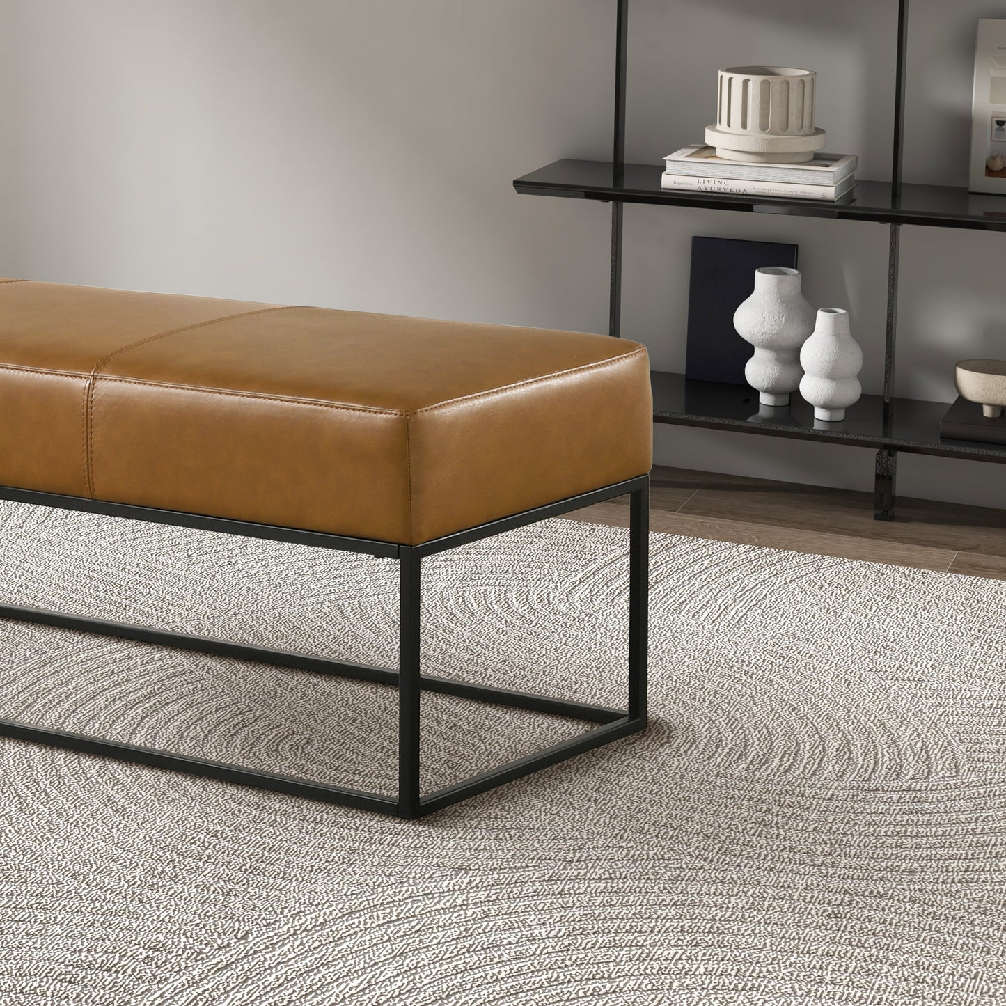 Modern tan leather bench with black metal frame on textured rug, home decor on shelves