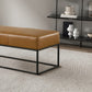Modern tan leather bench with black metal frame on textured rug, home decor on shelves