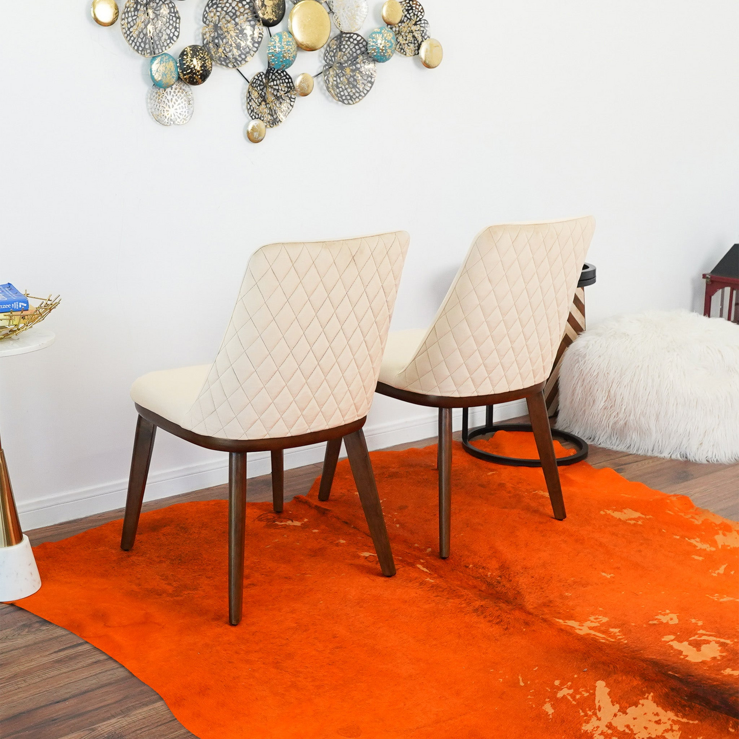 Modern dining room with two cream quilted chairs, orange rug, metal wall art decor, and wood flooring