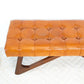Tufted brown leather bench with wooden legs on a white textured rug, FredCo International furniture