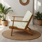 Mid-century modern wooden armchair with cream cushion on round rug, indoor plants, bright room
