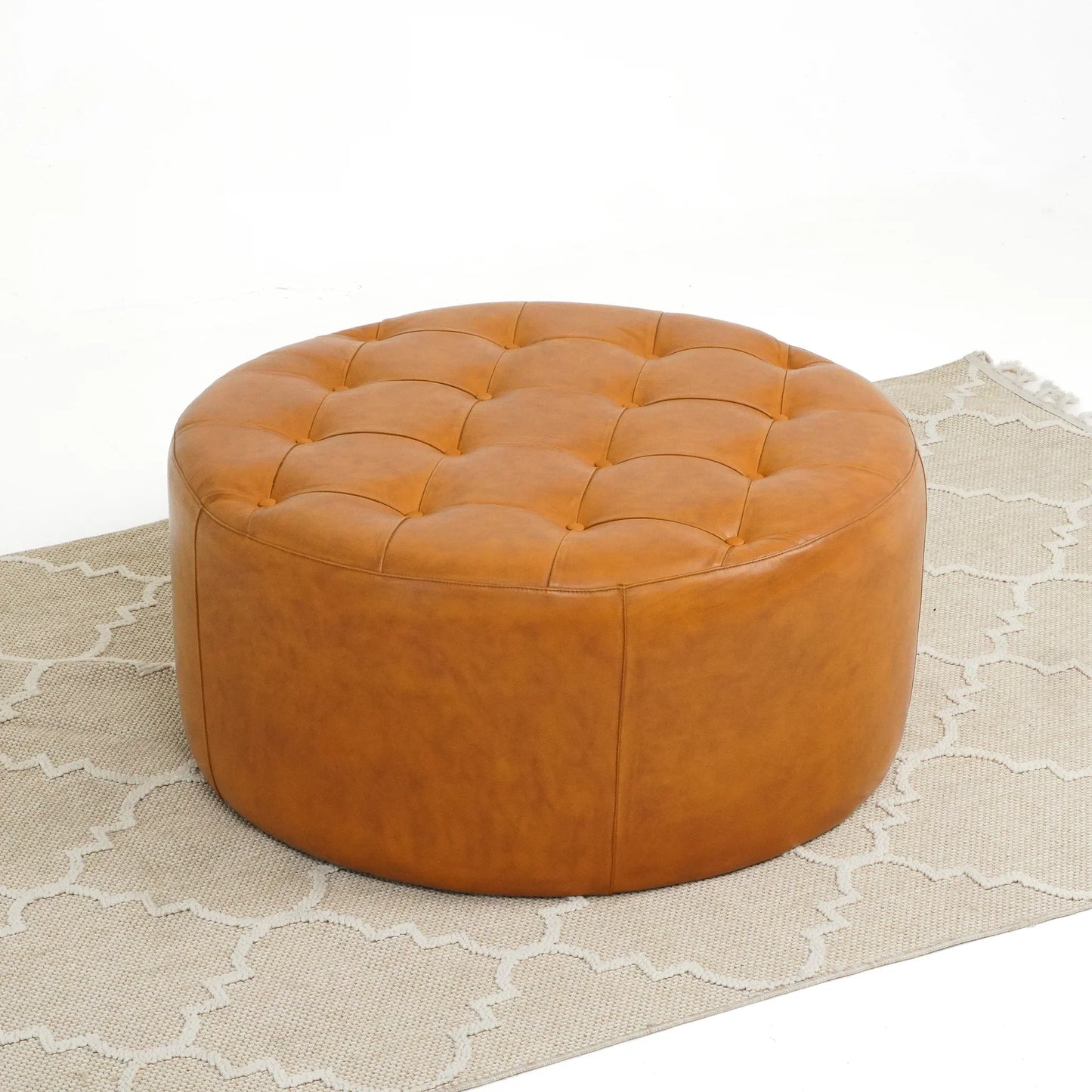 Round tufted brown leather ottoman on beige patterned rug, modern living room furniture