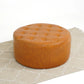 Round tufted brown leather ottoman on beige patterned rug, modern living room furniture