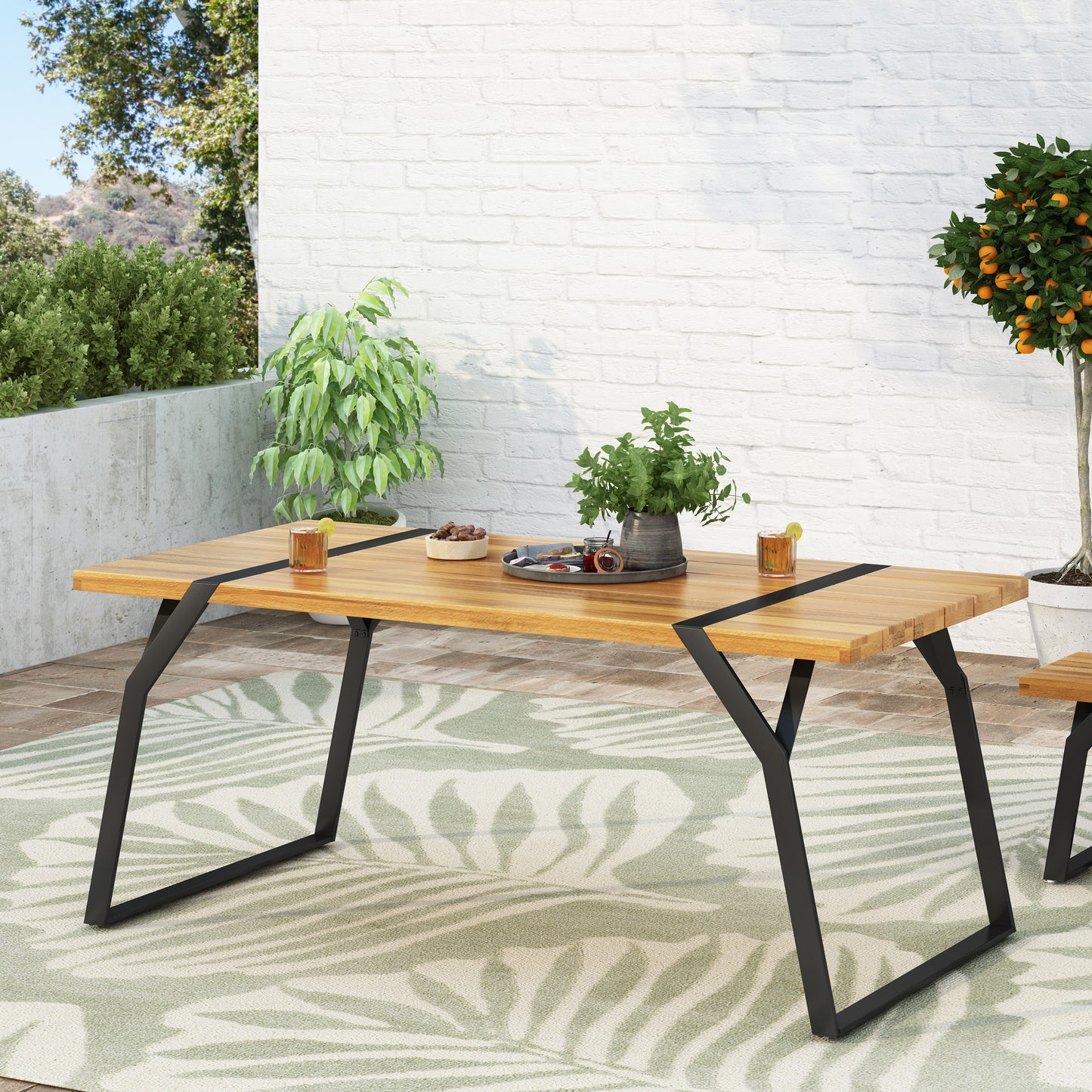Modern outdoor wood dining table with black metal legs on patio with plants and drinks