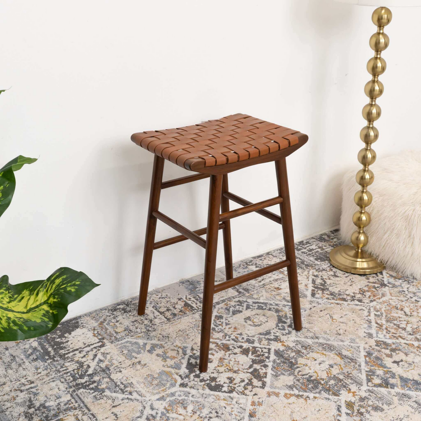 Mid-century modern brown woven stool on patterned rug near gold floor lamp and plush cushion