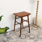 Mid-century modern brown woven stool on patterned rug near gold floor lamp and plush cushion