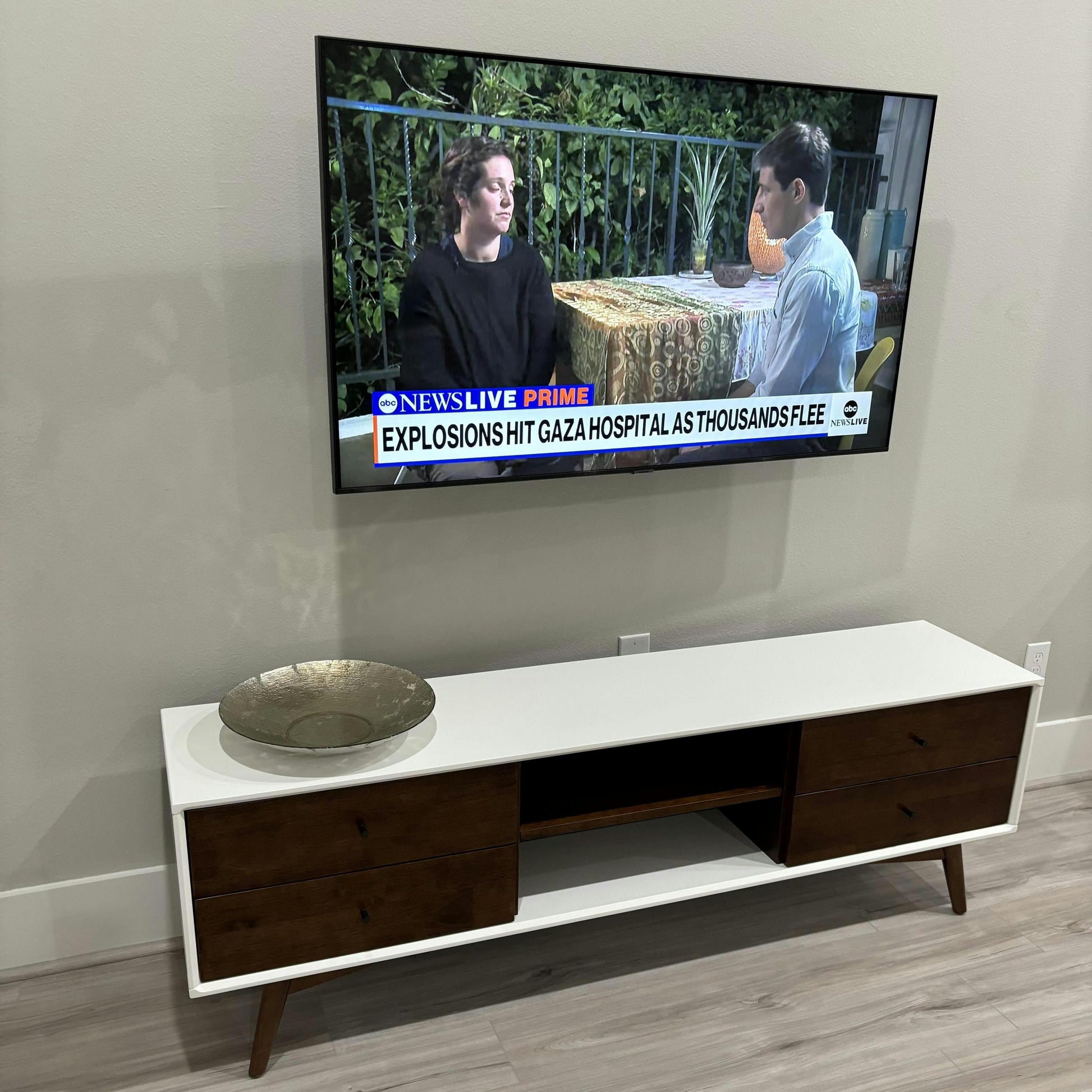 Modern white and wood TV stand with metal bowl, flat-screen TV mounted above, home furniture.