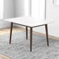 Modern square dining table with white top and wooden legs on patterned rug in bright room
