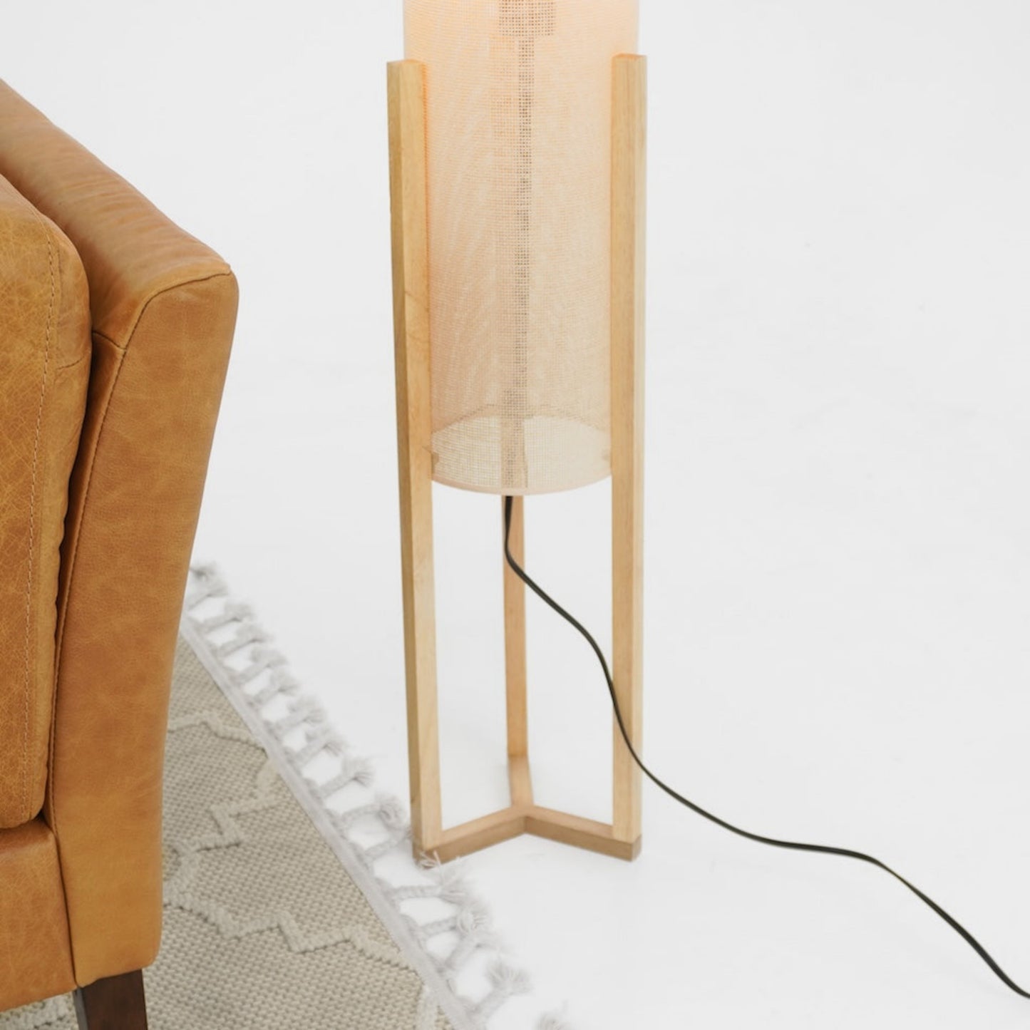 Modern wooden floor lamp beside tan leather sofa and fringed area rug, FredCo International furniture