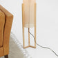 Modern wooden floor lamp beside tan leather sofa and fringed area rug, FredCo International furniture