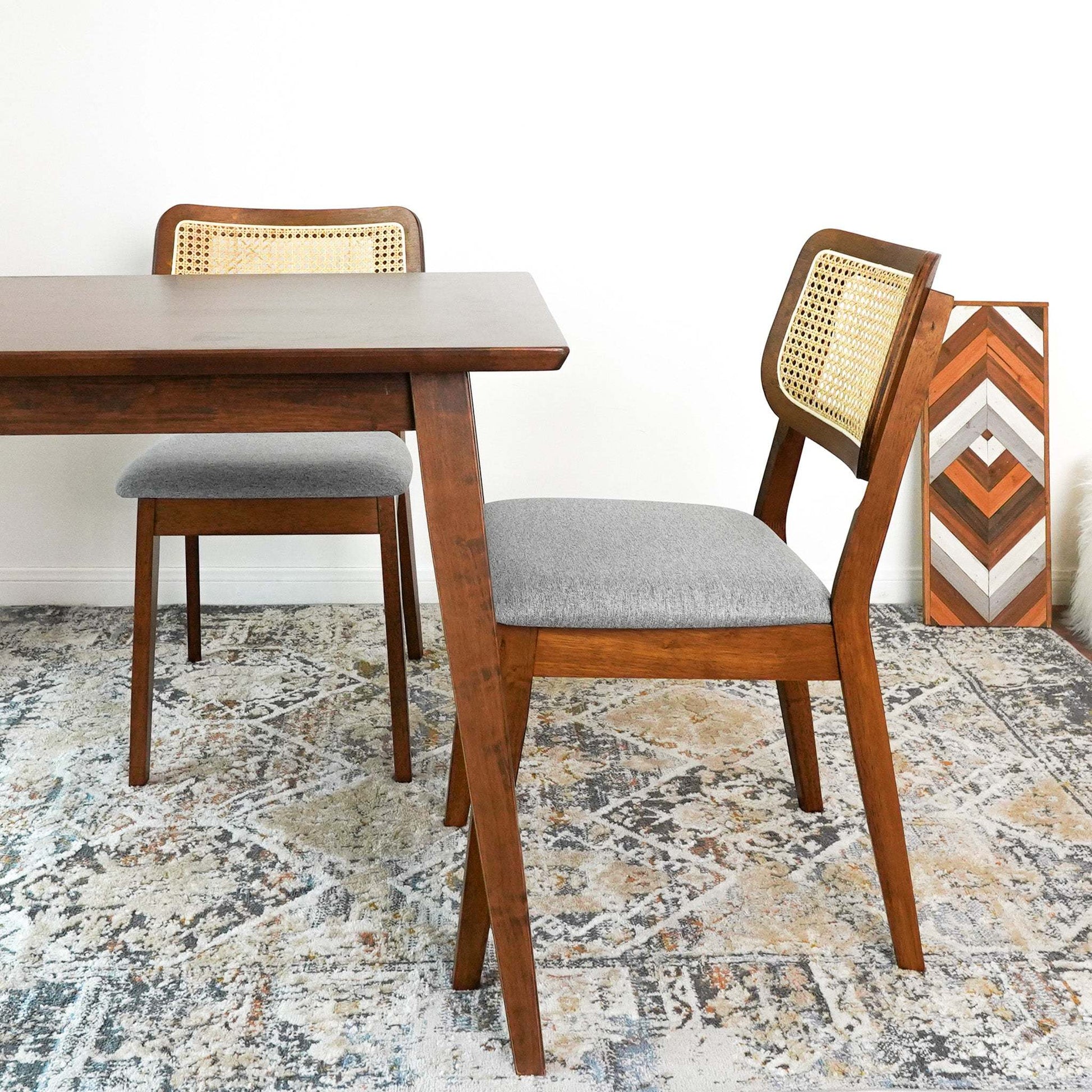 Modern wood dining chairs with cane backs and gray cushions beside a table on patterned rug