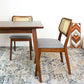 Modern wood dining chairs with cane backs and gray cushions beside a table on patterned rug