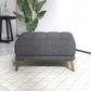Modern gray upholstered ottoman with wooden legs on a patterned rug in a stylish living room