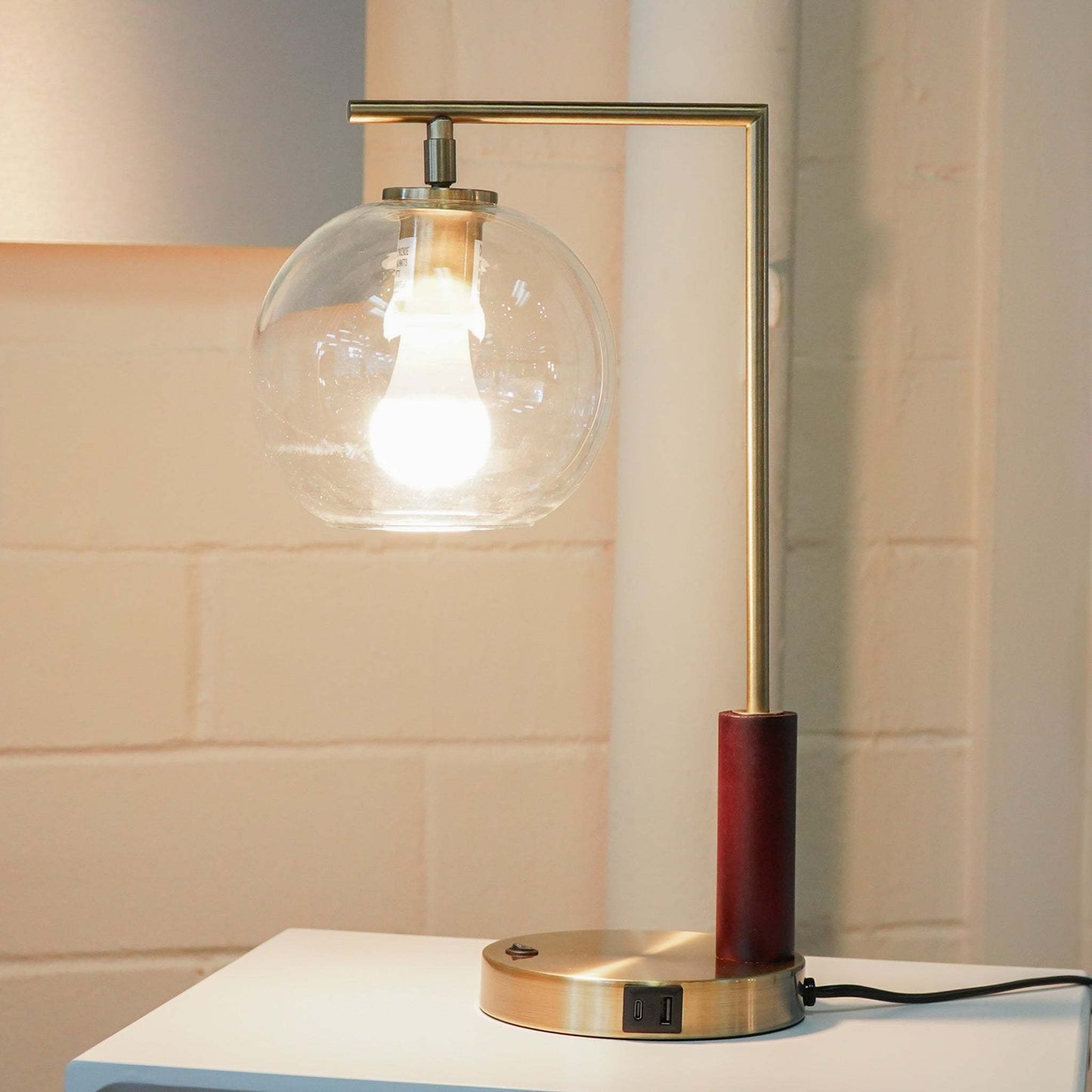 Modern brass table lamp with clear glass globe shade on white side table, stylish home decor