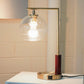 Modern brass table lamp with clear glass globe shade on white side table, stylish home decor