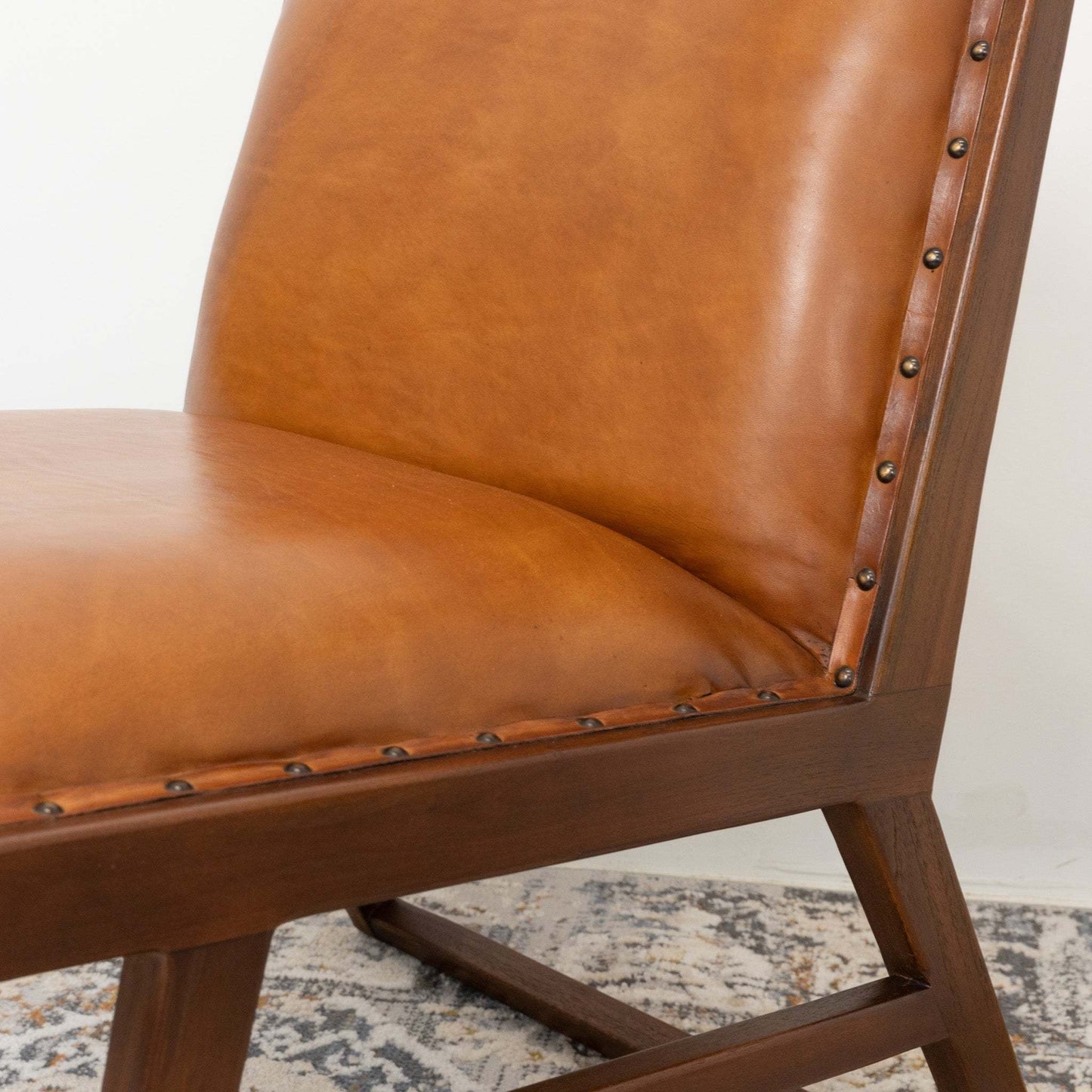 Brown leather dining chair with wood frame and nailhead trim on patterned rug