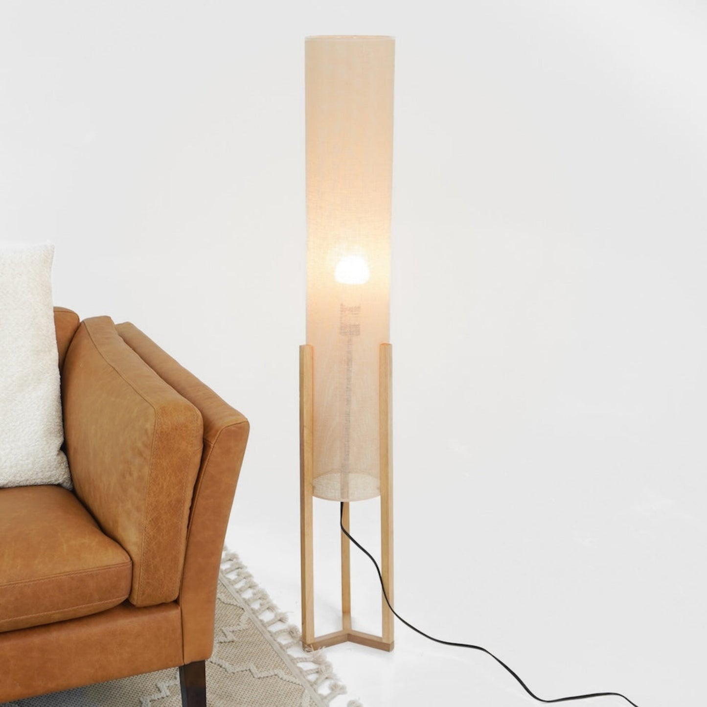 Modern tan floor lamp with fabric shade beside brown leather sofa and rug, FredCo furniture