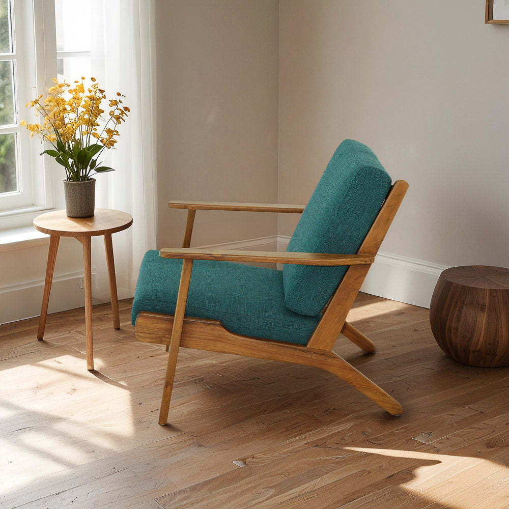 Modern teal lounge chair with wooden frame next to round side table and yellow flowers by window