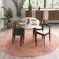 Modern dining room with round wood table, four chairs, pink rug, plants, and sideboard