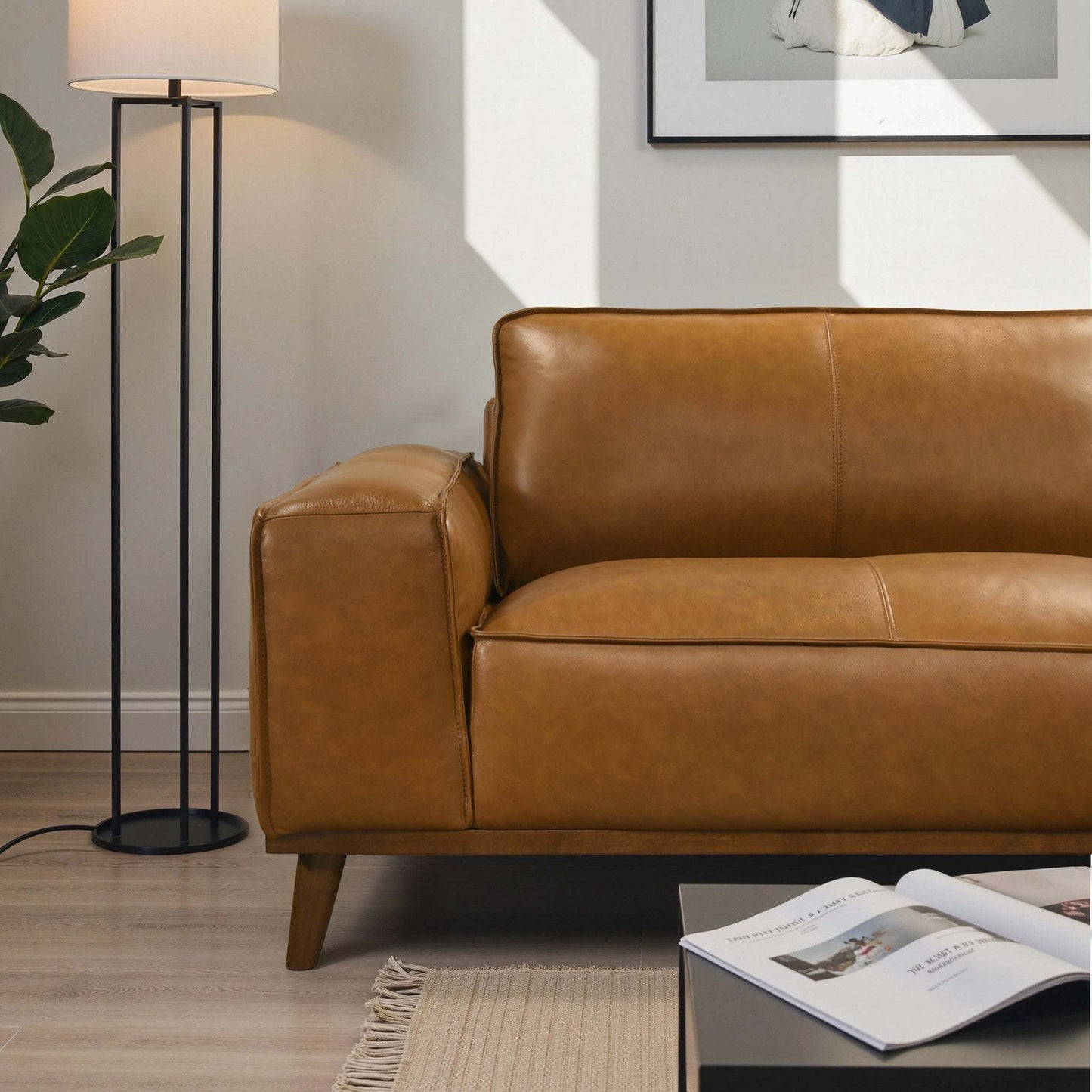 Modern tan leather sofa in living room with floor lamp, art, and coffee table, FredCo International furniture