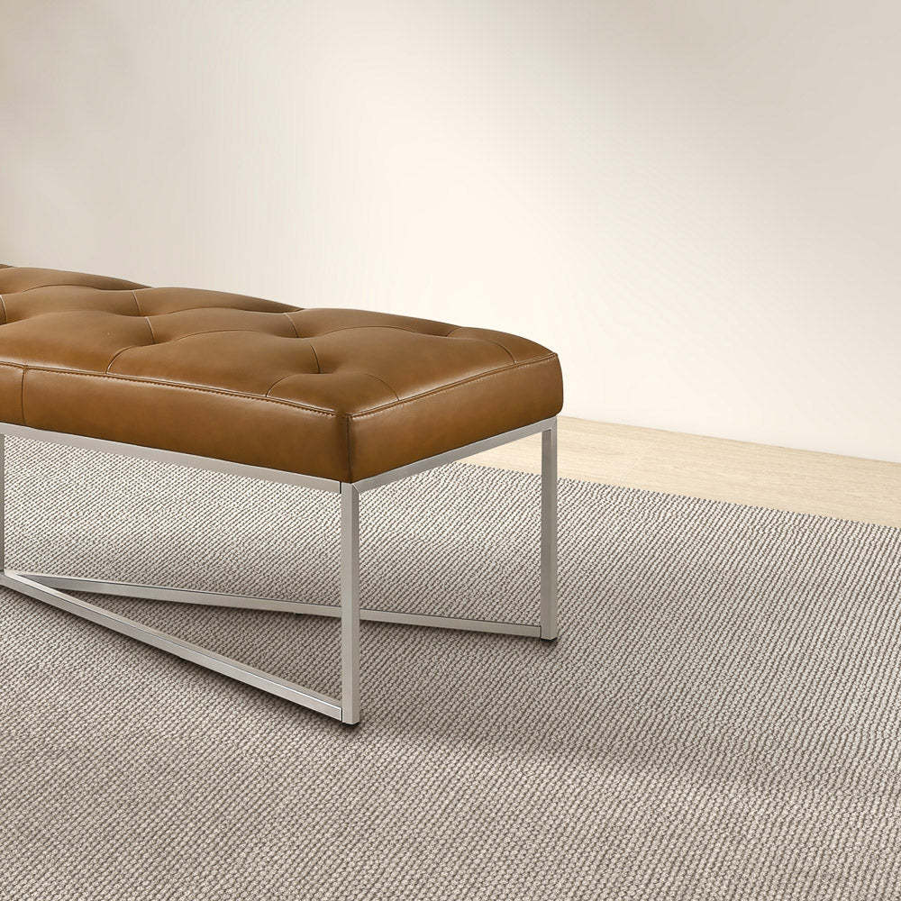 Modern brown leather bench with metal legs on a textured rug in a minimalist room