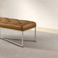 Modern brown leather bench with metal legs on a textured rug in a minimalist room