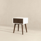 Mid-century modern nightstand with white frame, dark wood drawer, and angled legs on neutral background