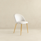 Modern white upholstered dining chair with gold legs on a neutral background, FredCo International furniture
