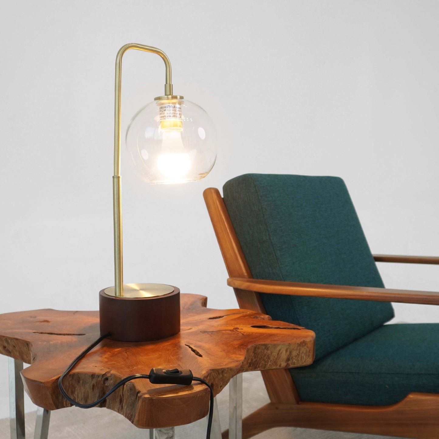 Modern glass globe table lamp on natural wood side table beside teal upholstered chair